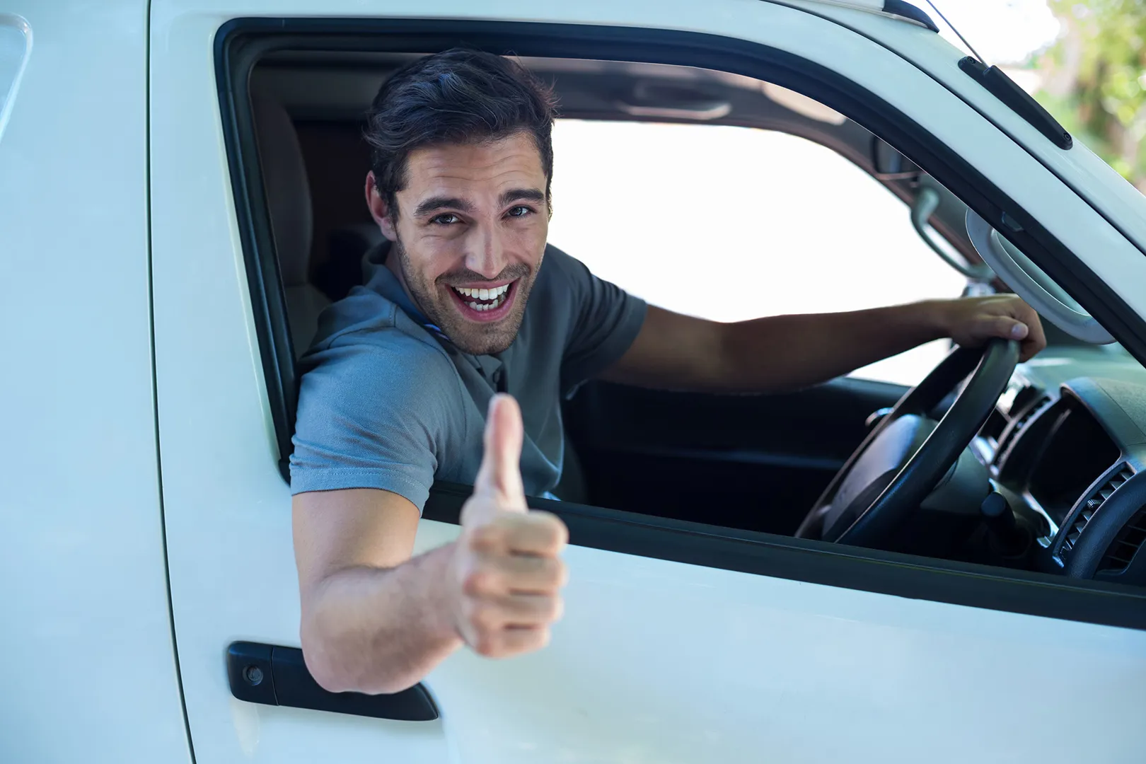 A man with a cheerful expression drives a white van, radiating happiness as he navigates the road.
