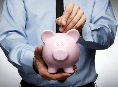 A man in a blue shirt and tie deposits money into a piggy bank, saving for the future.