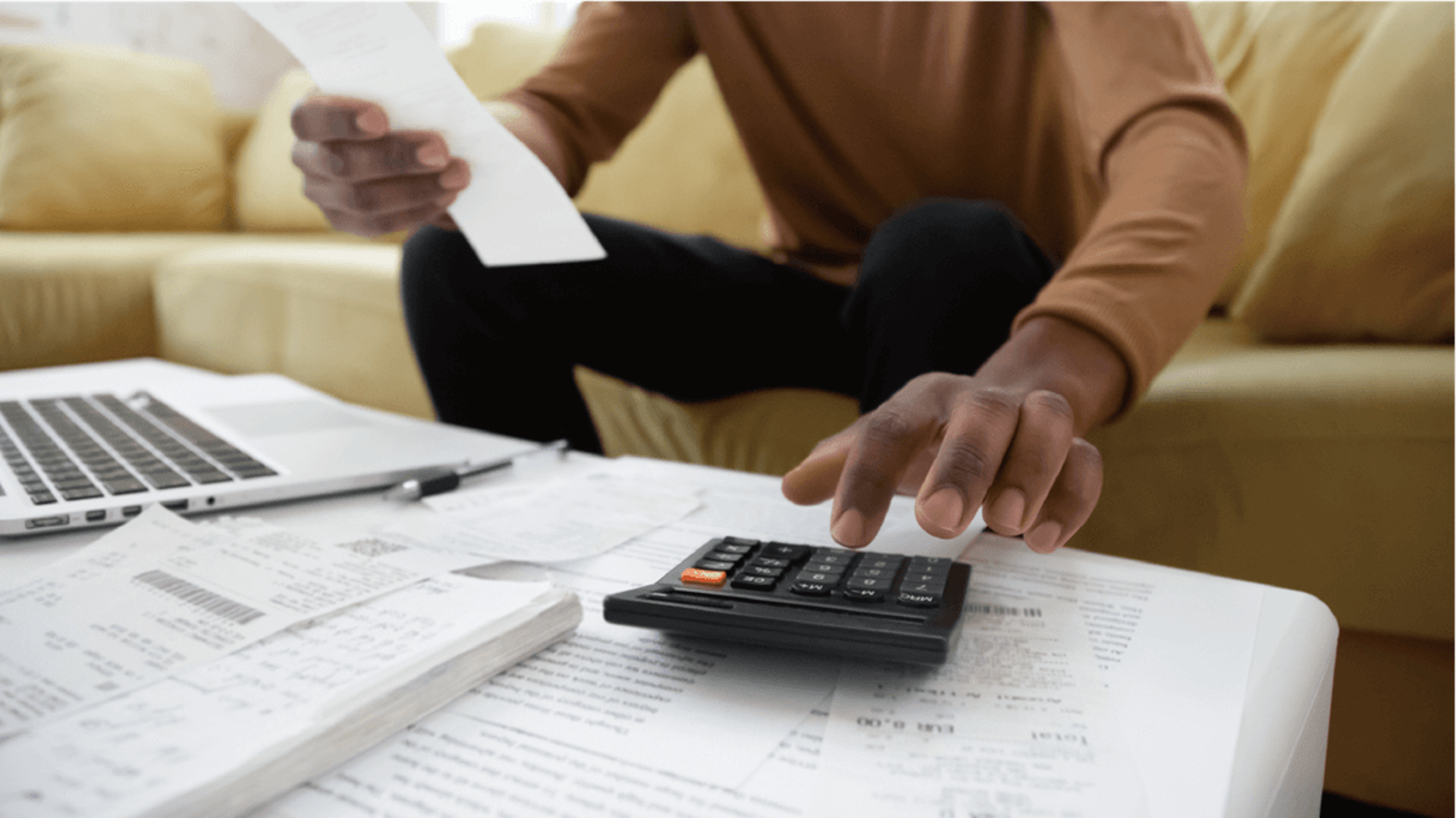 Man on sofa looking at papers, using calculator