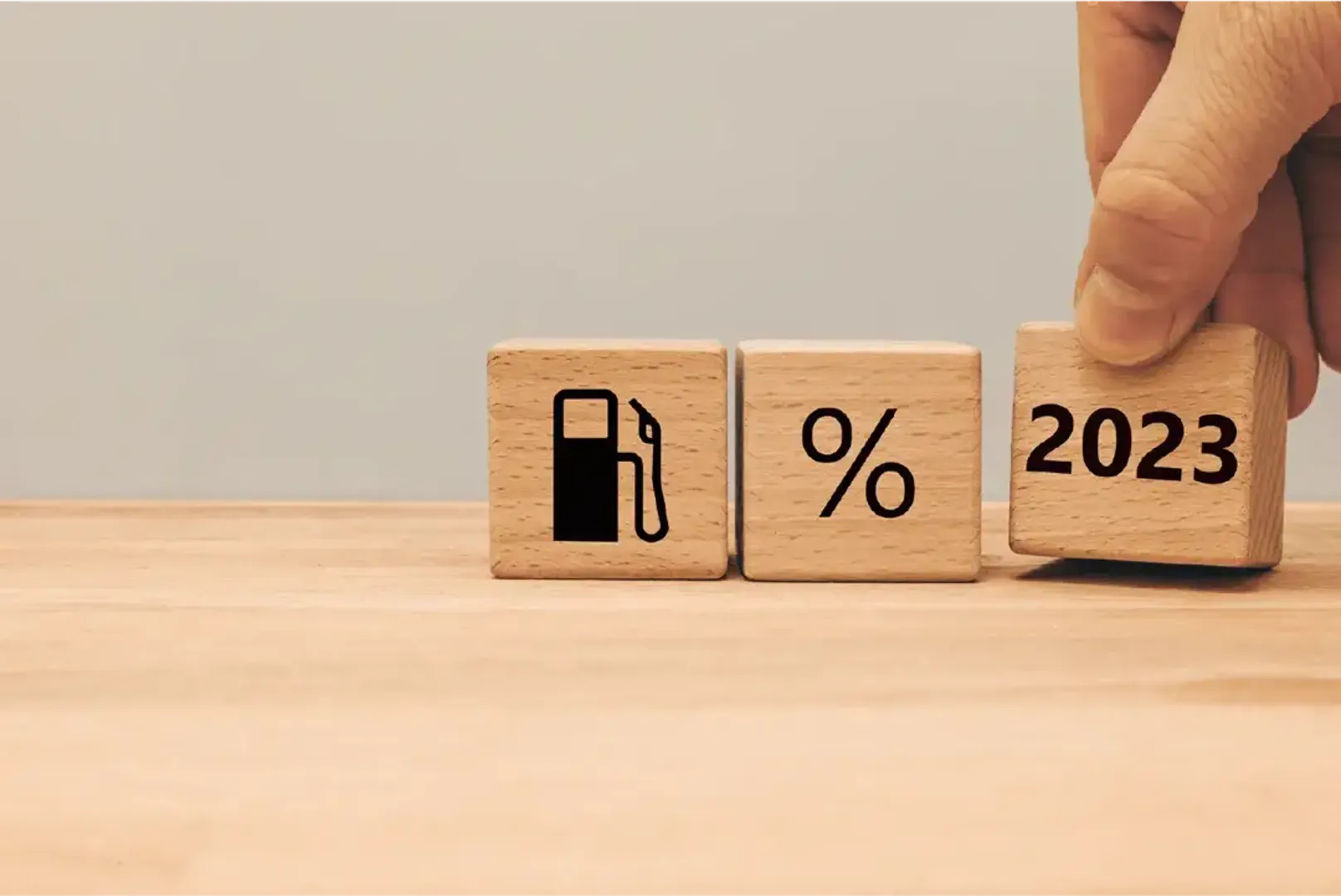 A person holding a wooden block with the words "2023" and a gas pump.