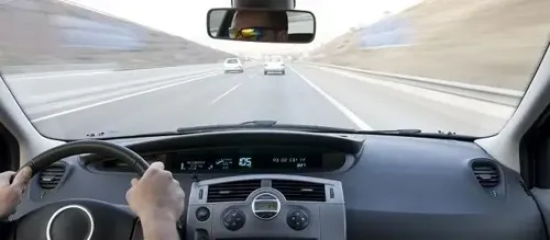 A person driving a car on the highway, focused and attentive, with other vehicles passing by.
