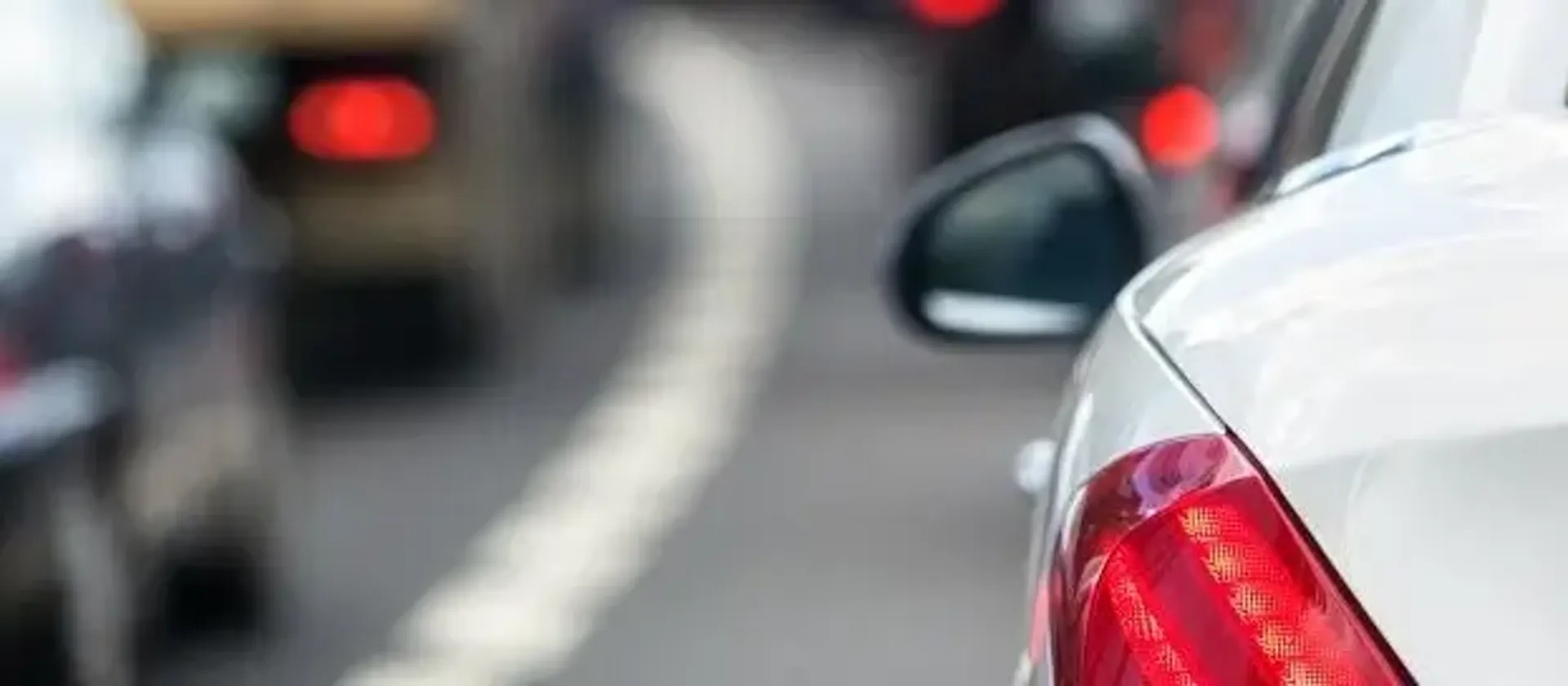 Cars queuing on the road in traffic with brake lights on. 