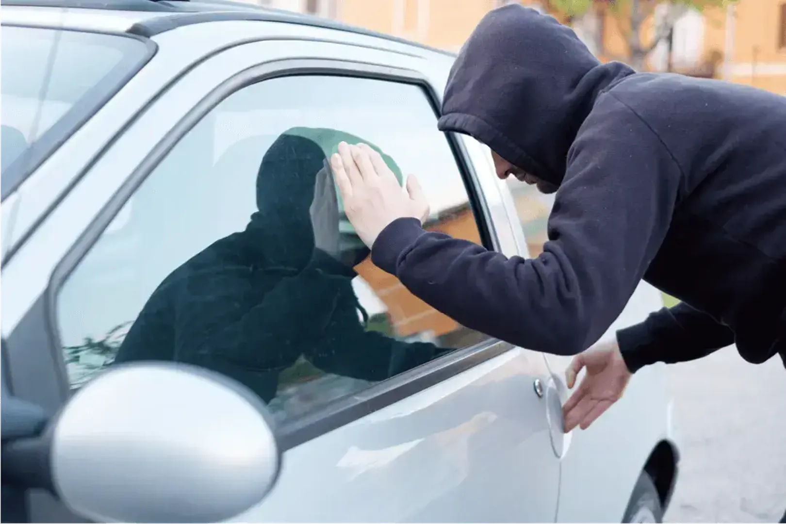 Man in hoodie peers through car window.