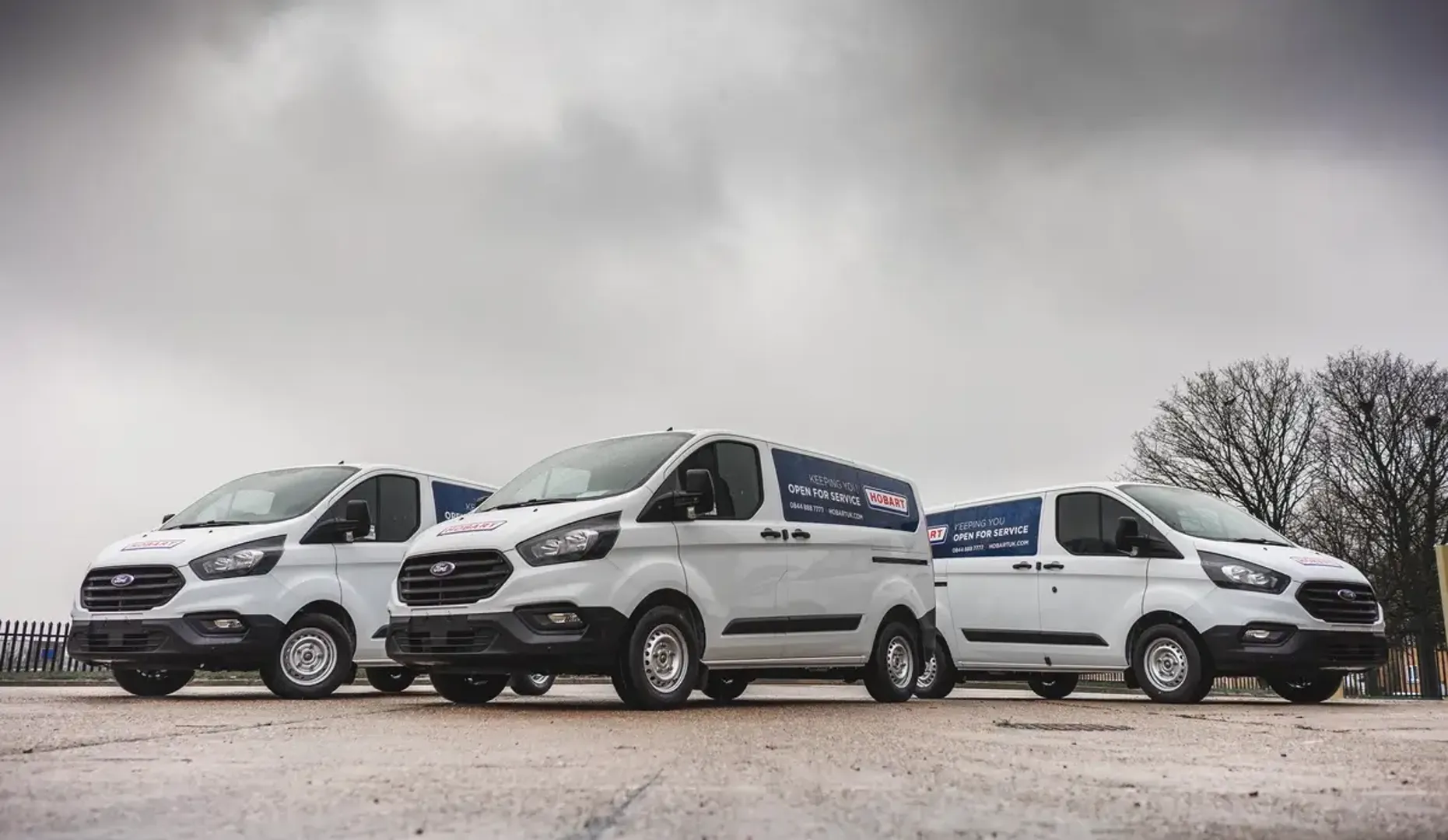 Three white vans parked in front of a cloudy sky.