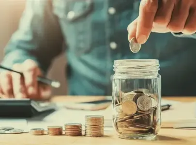 A man carefully placing coins into a jar on a desk.