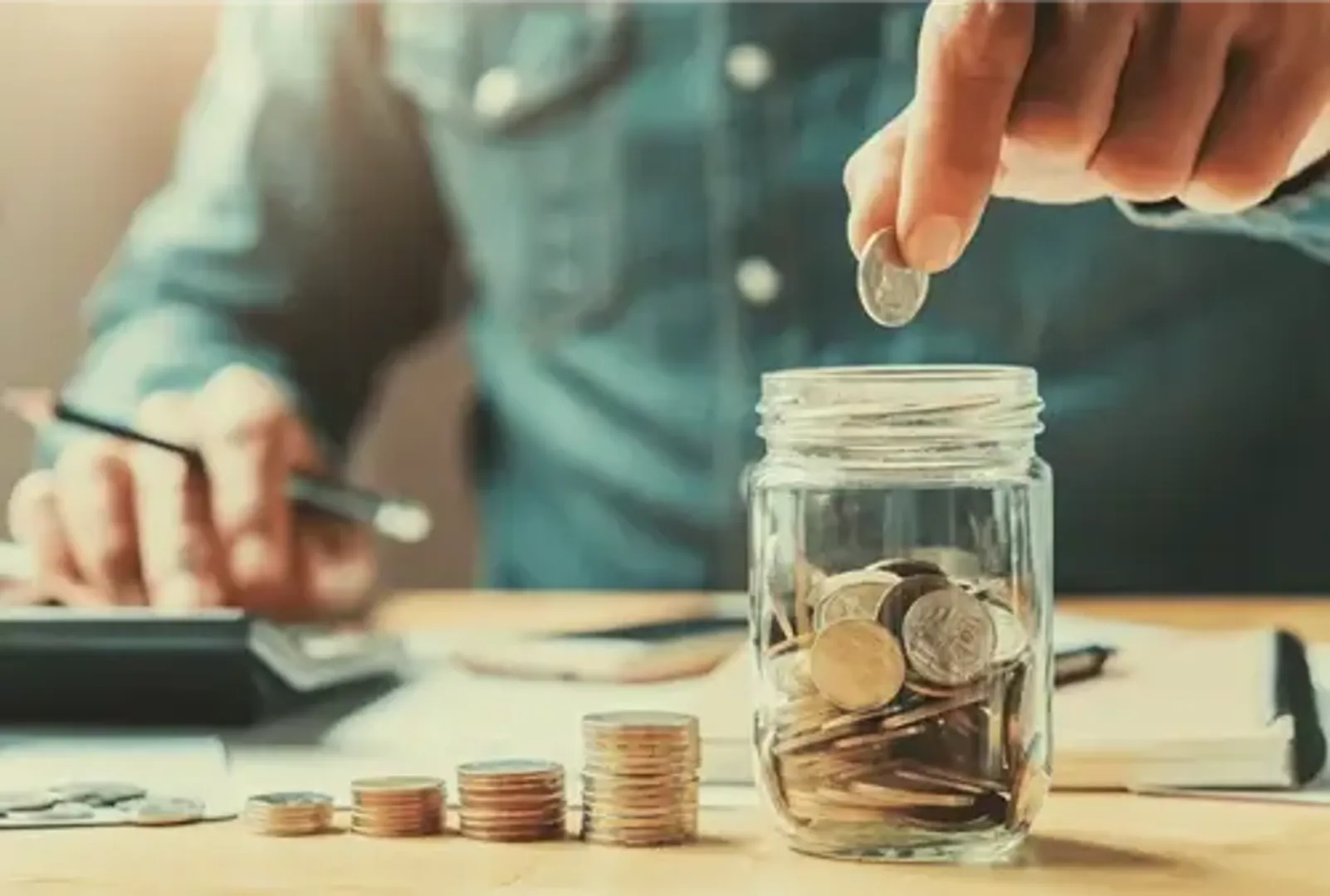 A man carefully placing coins into a jar on a desk.