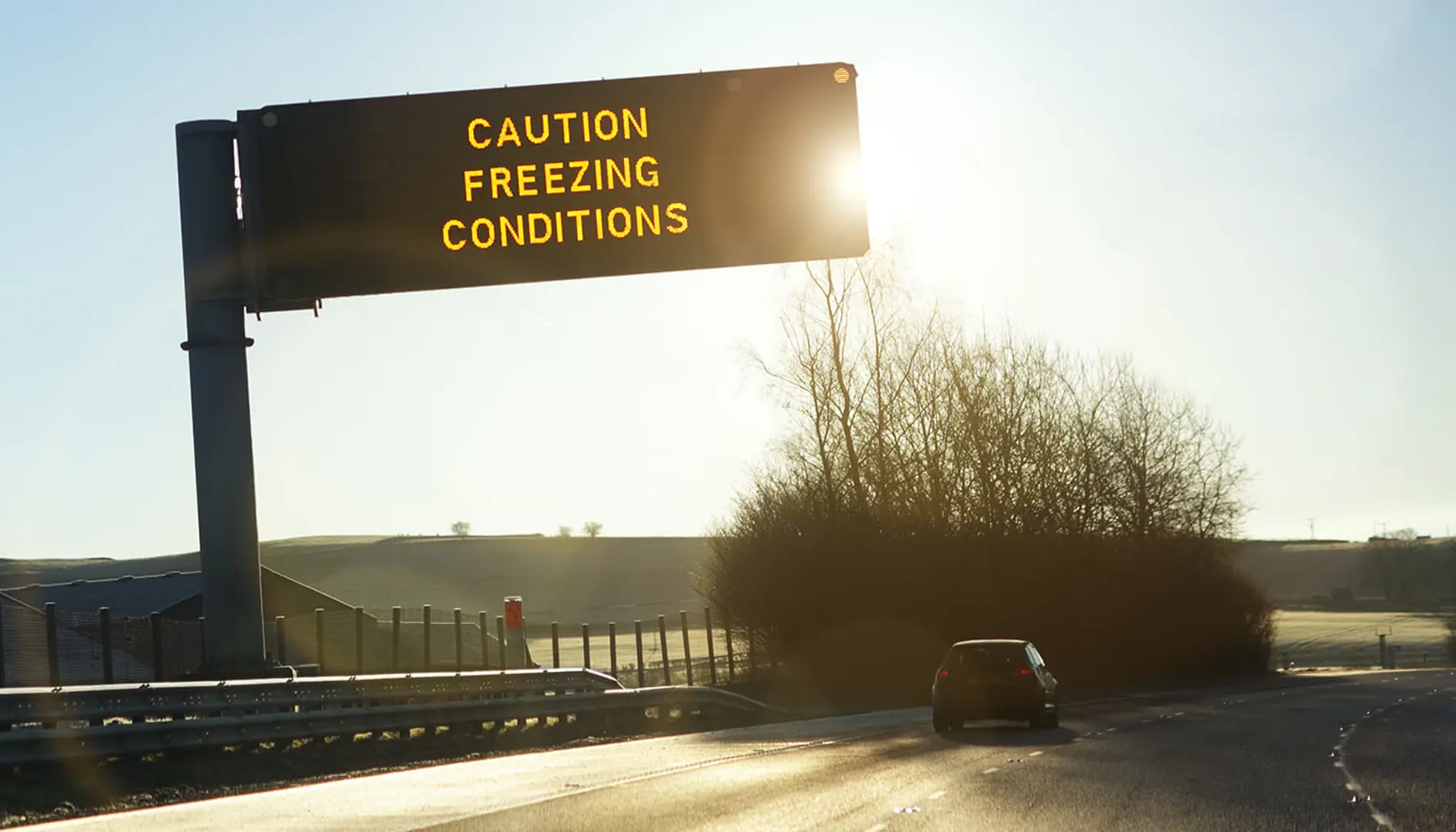 Road in cold conditions with a digital sign saying 'CAUTION FREEZING CONDITIONS'