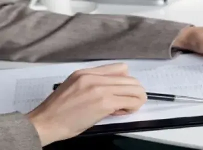 A professional woman in a business suit diligently writes on a clipboard, focusing on her tasks.