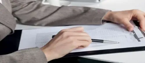 A professional woman in a business suit diligently writes on a clipboard, focusing on her tasks.
