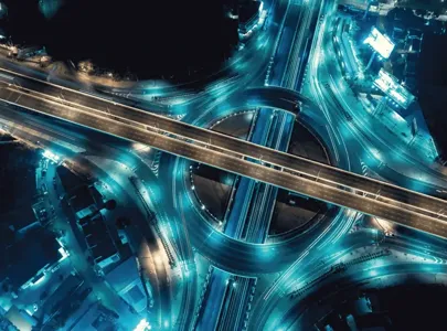 Aerial view of a highway intersection at night, showcasing the intricate network of roads and the vibrant city lights below.