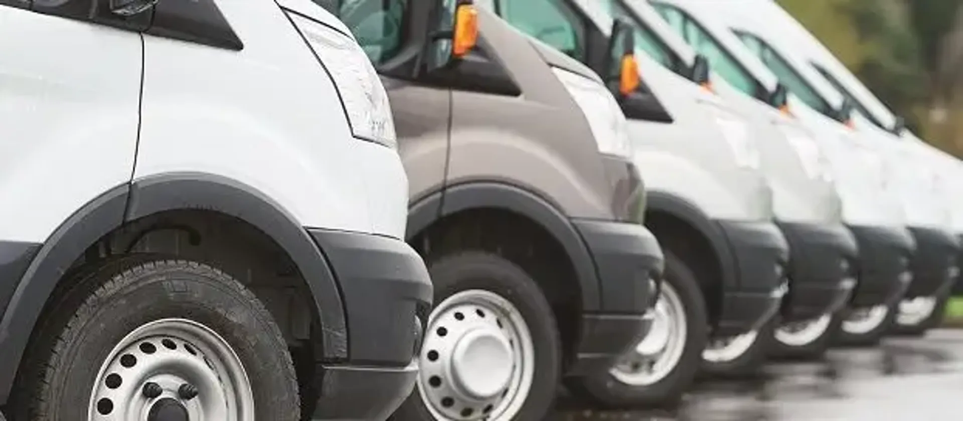 A lineup of white vans with only 1 being grey parked in a row.