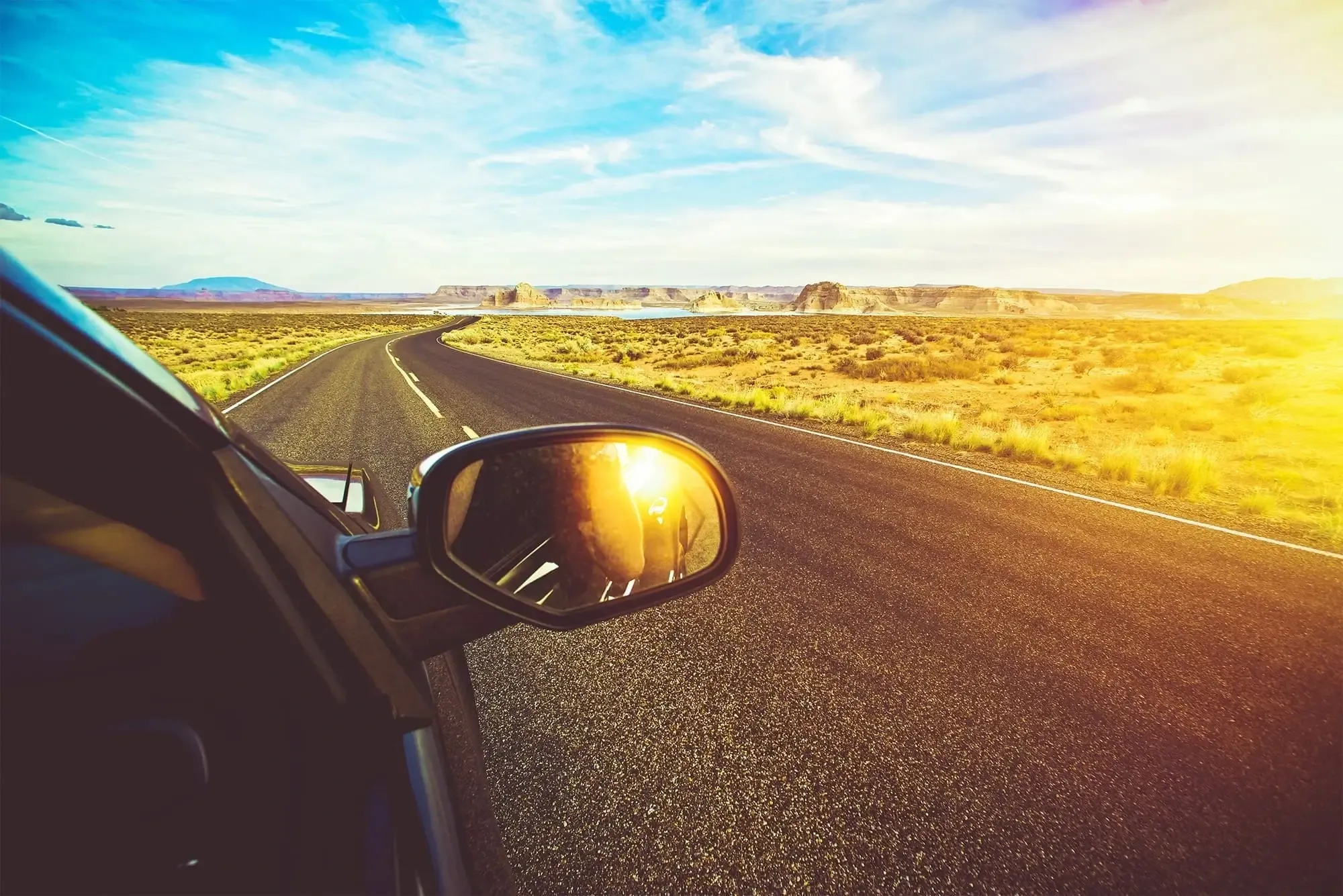 A car's side mirror reflects a desert landscape during a road trip, showcasing the vastness and beauty of the arid terrain.
