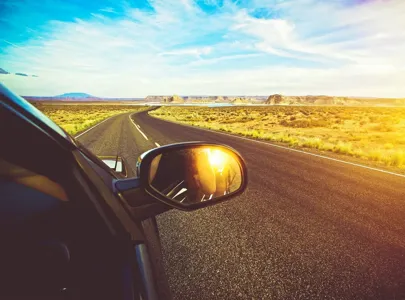 A car's side mirror reflects a desert landscape during a road trip, showcasing the vastness and beauty of the arid terrain.