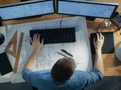A man focused on his computer screen while examining blueprints for a project.