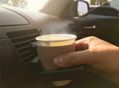 A person driving with one hand on the steering wheel and the other holding a cup of coffee.