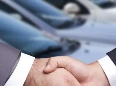 Two men shaking hands in front of a car, symbolising a successful business deal.