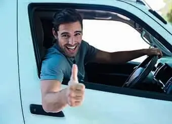 A man with a cheerful expression drives a white van, radiating happiness as he navigates the road.