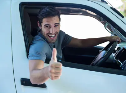 A man with a cheerful expression drives a white van, radiating happiness as he navigates the road.