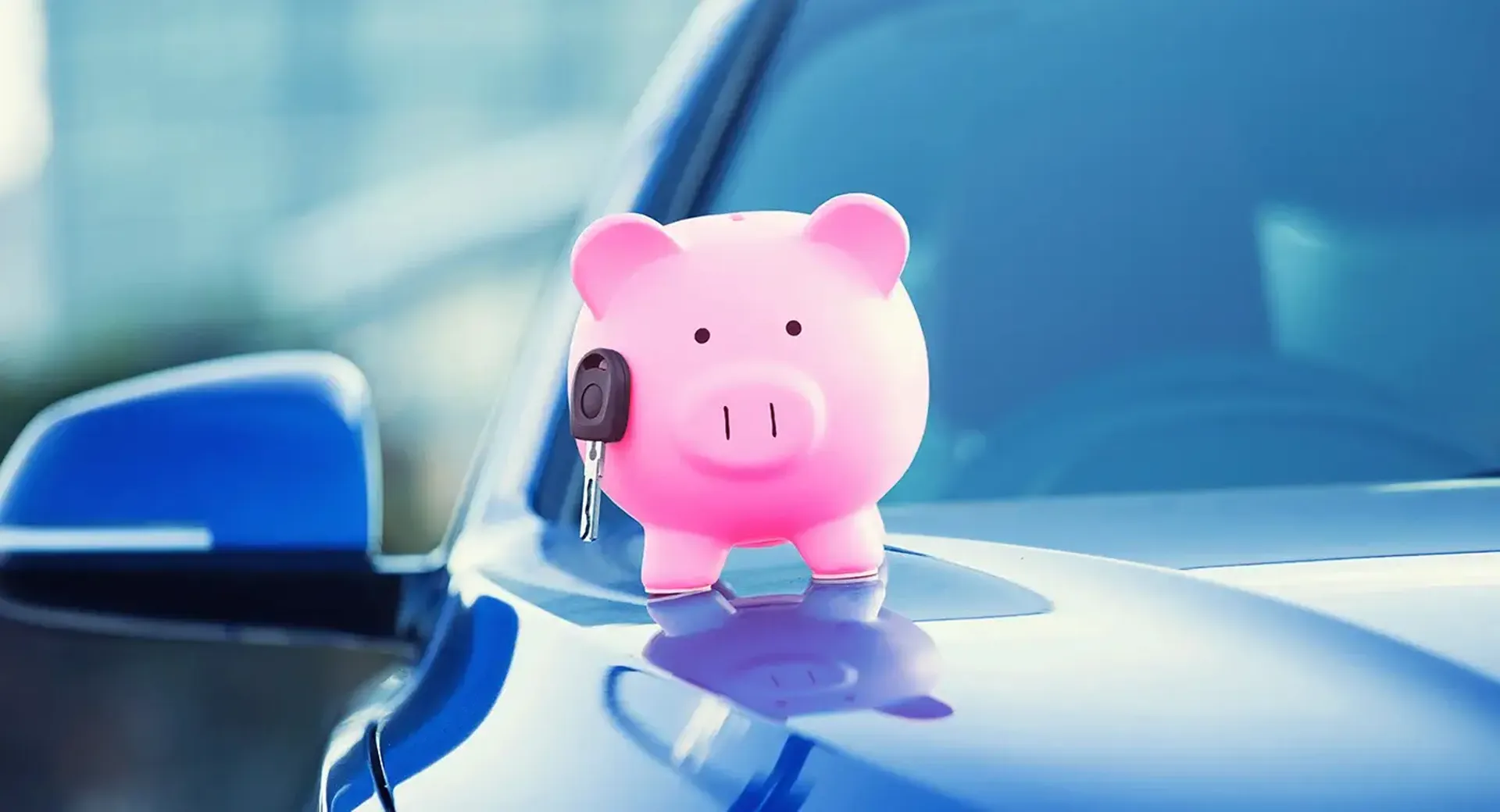 A pink piggy bank sits on a car with car keys nearby.