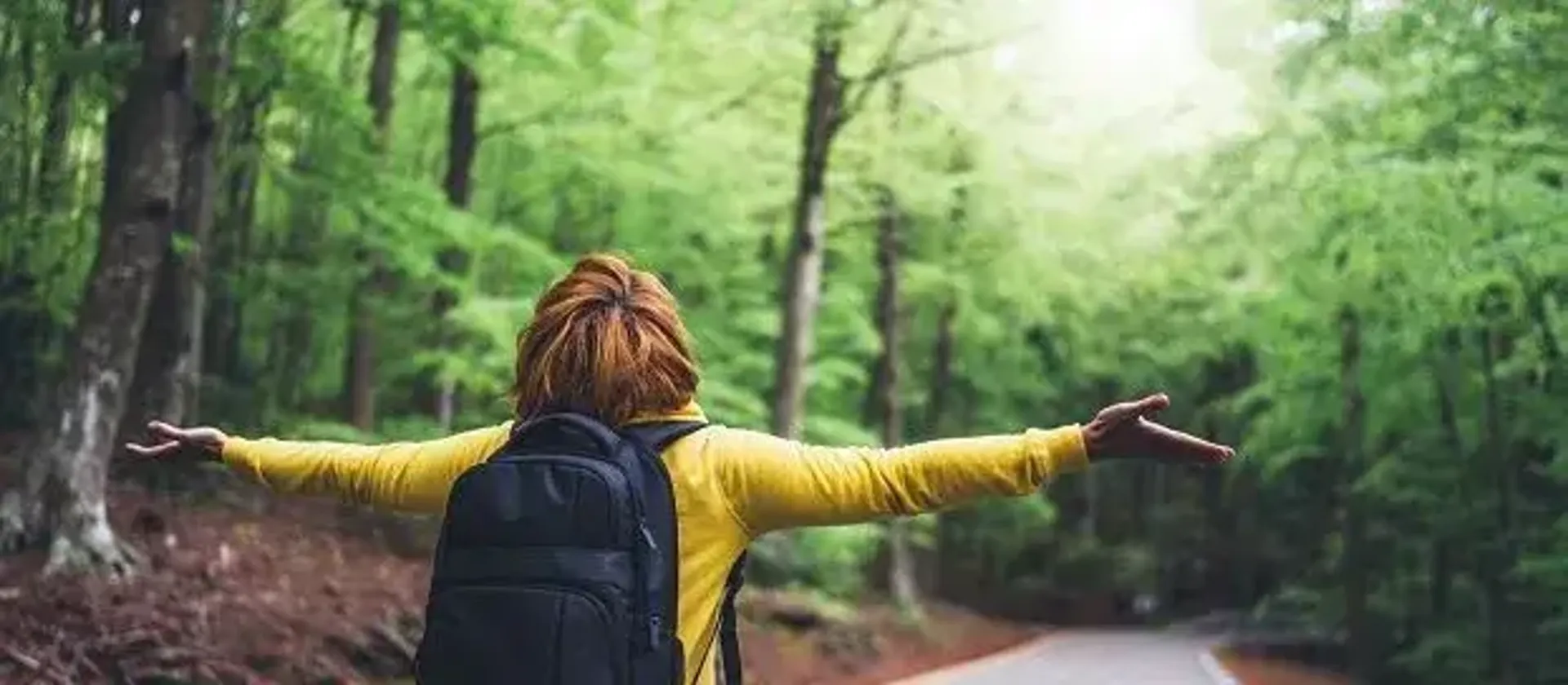 Person standing in a forest, arms spread looking up at the sky.