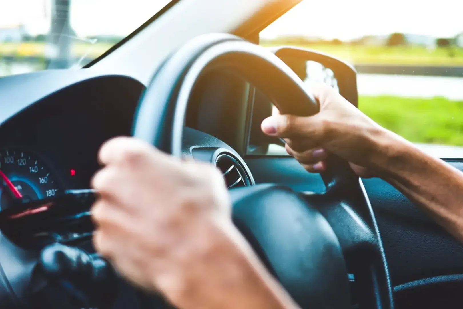 Both hands of a person on the steering wheel of a car