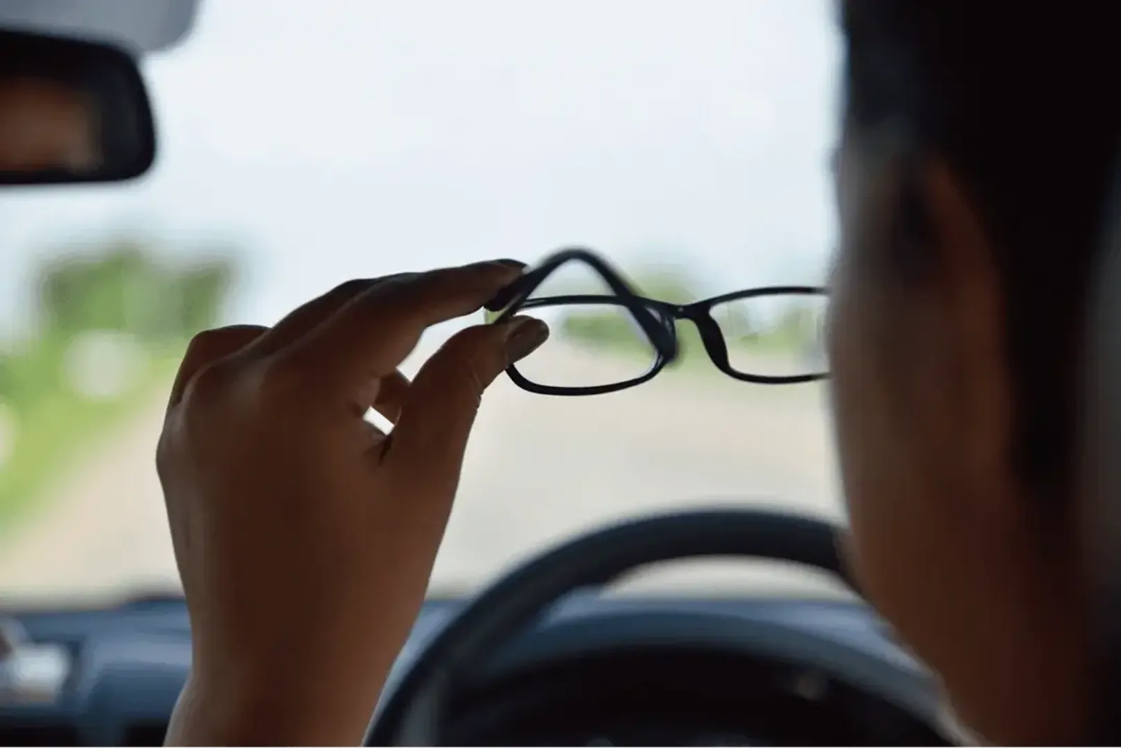 Person in the driving seat of a car putting their glasses on.