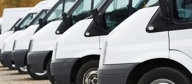A line of white vans parked in a parking lot, ready for transportation.