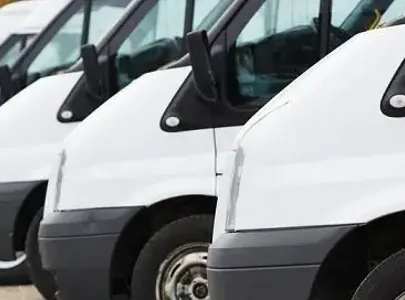 A line of white vans parked in a parking lot, ready for transportation.