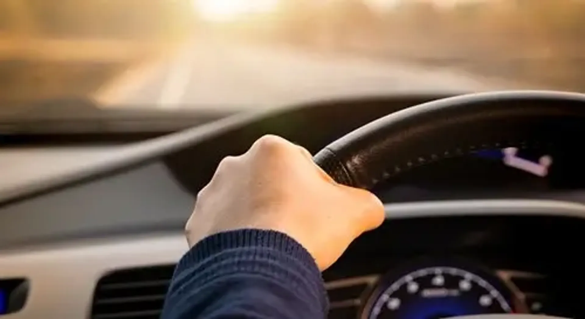 A person driving a car with one hand on the steering wheel, focused on the road ahead.