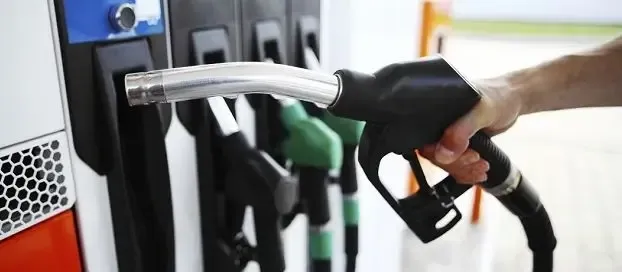 A person refuels their car at a gas station, holding the nozzle that they've picked up from the holder.