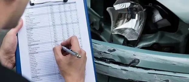 A man inspecting a damaged car, taking notes on a clipboard.